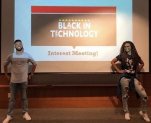 Charlie and a peer stand on either side of a projection screen showing the Black in Technology logo.