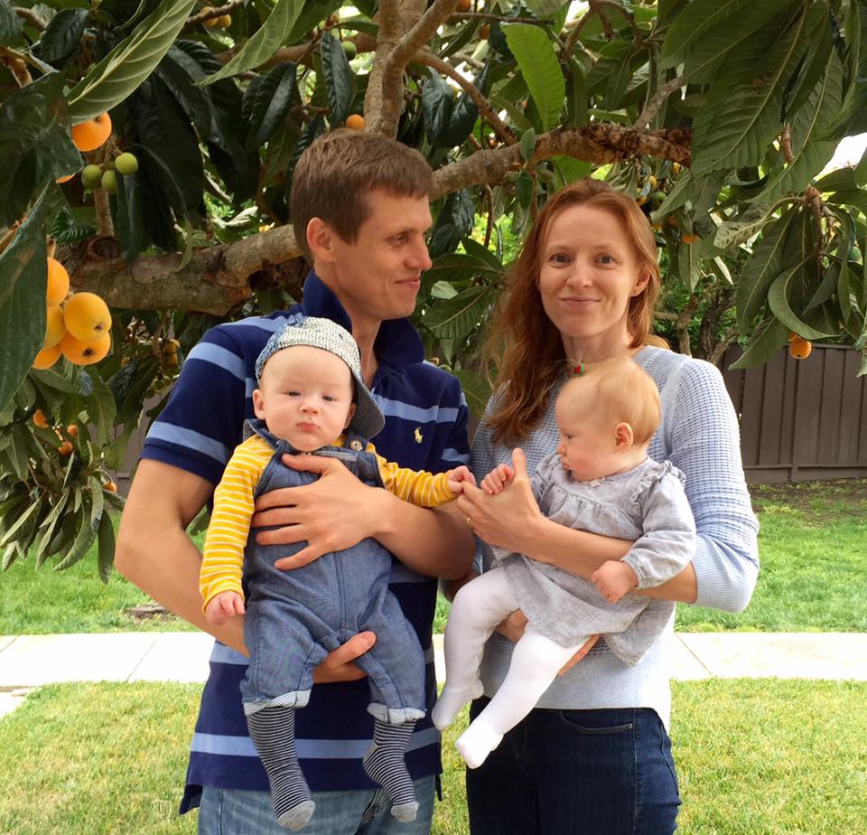 Andrey and his wife hold their two children in front of an orange tree.