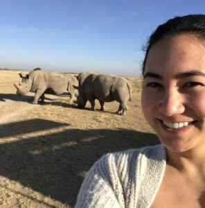 Cayla takes a selfie with two rhinos in the desert.
