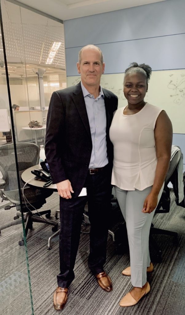 Daija stands smiling next to our SVP of Supply Chain, John Kern in the office.