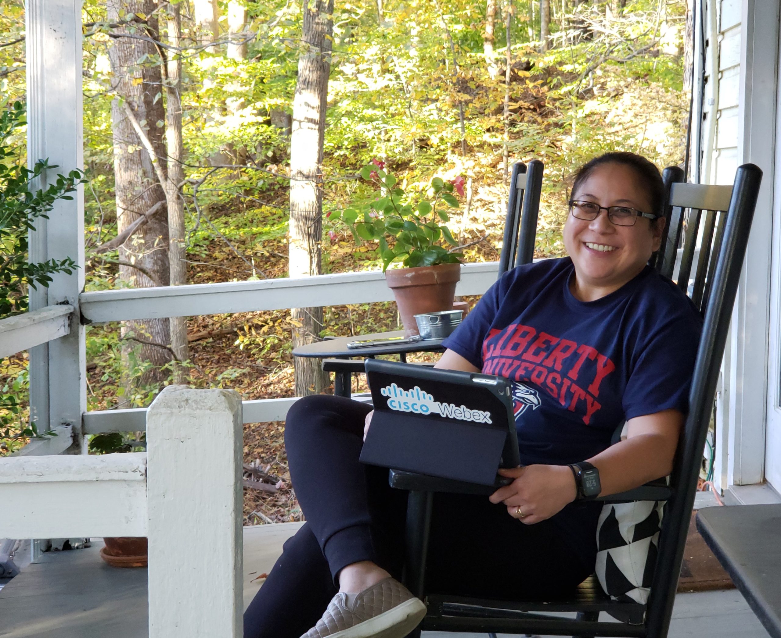 Maria sits outside in a rocking chair with an iPad for school while wearing a Liberty University shirt.