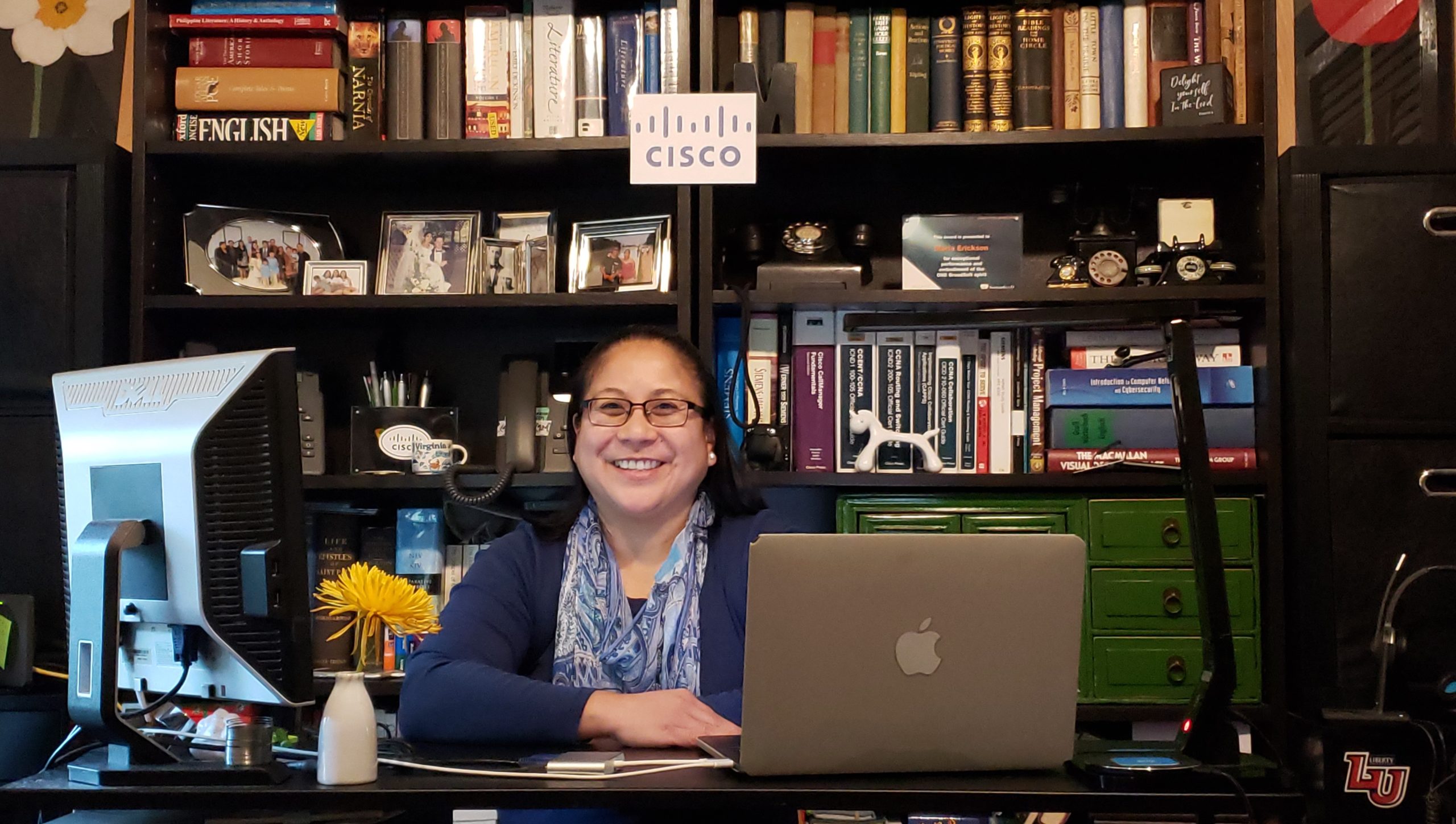 Maria smiles in front of bookcases and behind the desk in her home office.