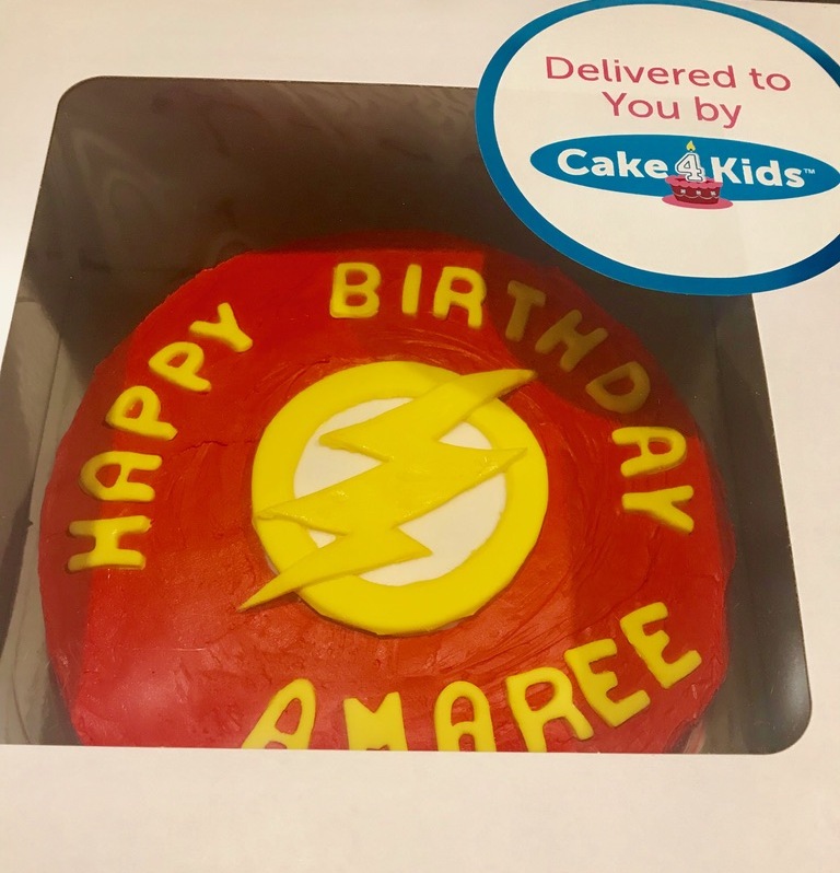 A red superhero cake with yellow writing that says 'Happy Birthday Amaree" and a lightning bolt in the center.