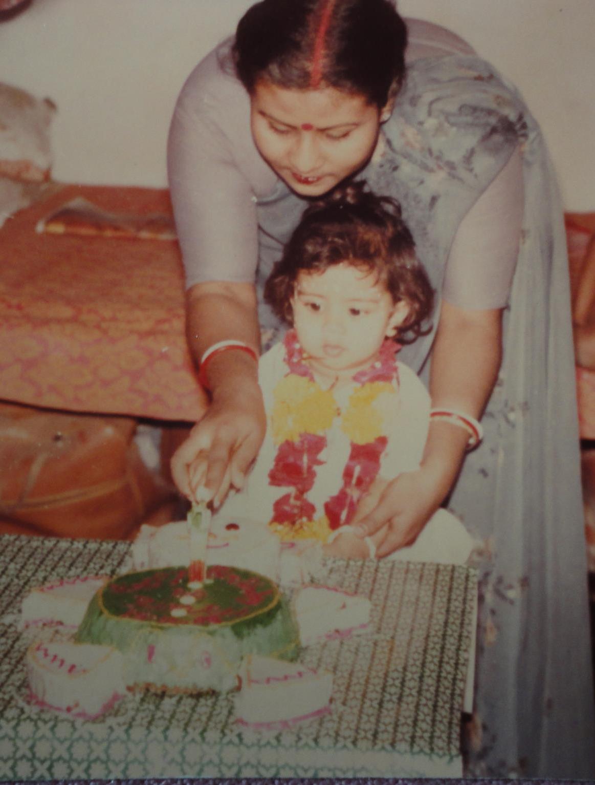 Mitali cutting the cake at her first birthday with the help of a family member.