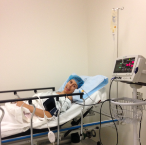 Joana lays in a hospital bed hooked up to medical equipment.