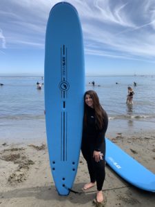 Rachel, on the beach with her surfboard.