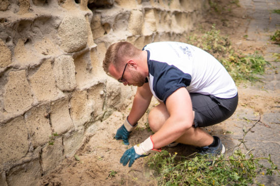 An employee kneels down, wearing gloves, as he helps weed the landscape.