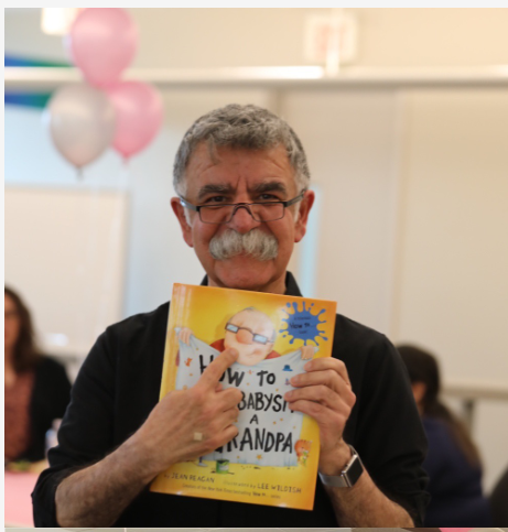 Ali shows his dinstinctive mustache and one of the gifts from his grandbaby shower, a book titled "How to Babysit a Grandpa".