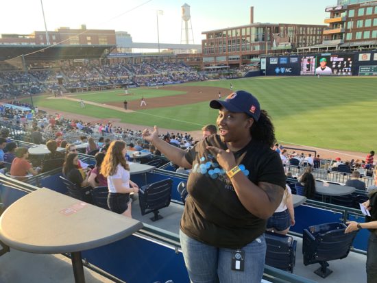 Leigh is showing some of her arm tattoo in a Cisco shirt while at a Durham Bulls baseball game.