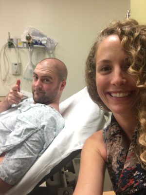 Dustin in a hospital gown and bed takes a picture with his then fiance from his hospital room.