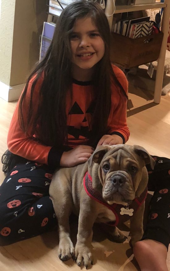 Danielle's daughter Helene sits in Halloween pajamas with their bulldog Winston.
