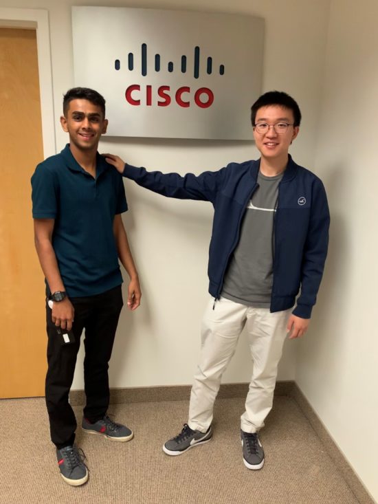 Dhwan standing with a colleague in front of a Cisco office sign.
