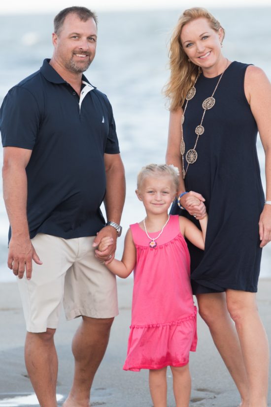 Erin smiles on the beach with her husband and daughter.