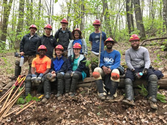 Emilio and his fellow interns wearing hard hats in the woods at a give back event.