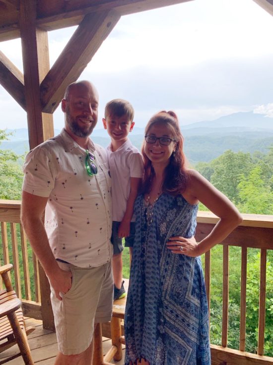 Bryan smiles with his family on a porch overlooking mountains.