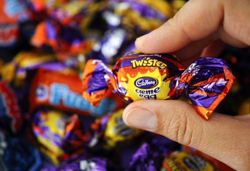 Paphos, Cyprus - November 27, 2015: Cadbury Twisted Creme Egg candy in womans hand with background of Cadbury candies.